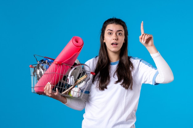 Vorderansicht junge Frau mit Korb voller Sport Dinge blaue Wand