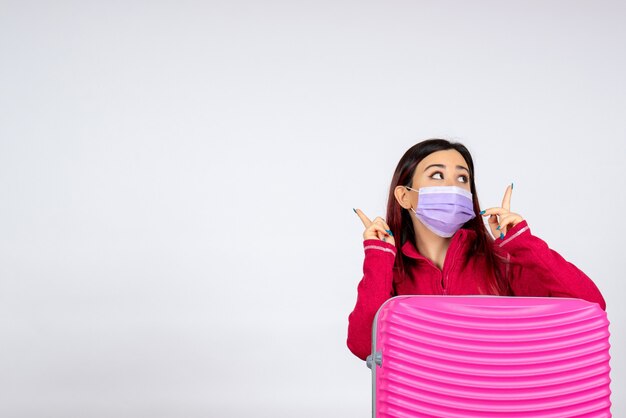Vorderansicht junge Frau mit rosa Tasche in Maske auf weißer Wand Virus Urlaub Covid Farbe Pandemie Reise