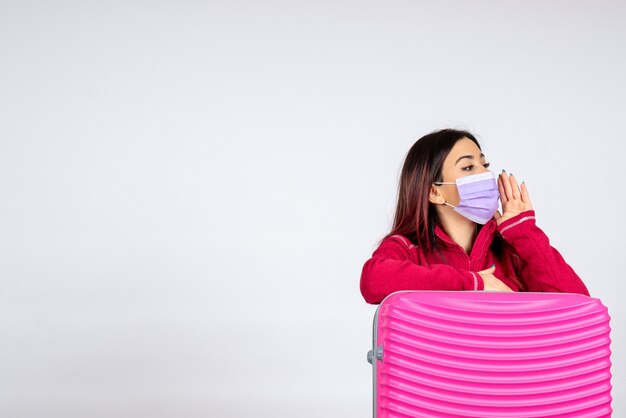 Vorderansicht junge Frau mit rosa Tasche in steriler Maske, die weiße Wandreisefarbferien-Covid-Frauenvirus-Pandemie anruft