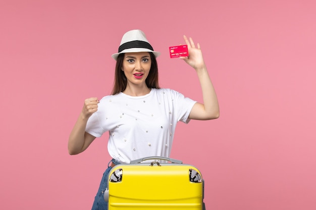 Vorderansicht junge Frau mit roter Bankkarte auf hellrosa Wandfarbe Reise Sommerreise