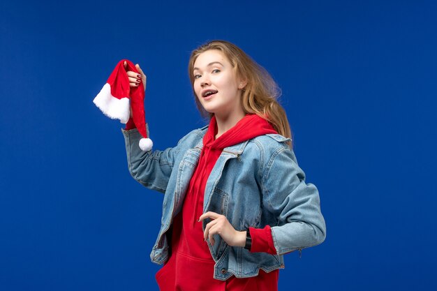 Vorderansicht junge Frau mit roter Kappe auf blauem Hintergrund Feiertage Weihnachten Neujahr