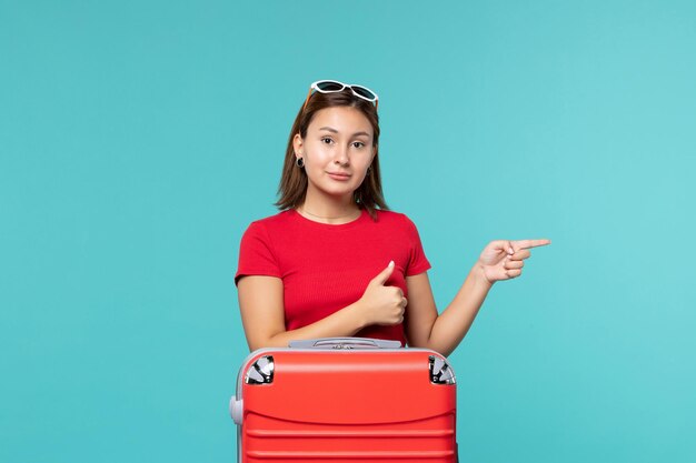Vorderansicht junge Frau mit roter Tasche, die für Urlaub auf blauer Bodenfarbreise-Reise-Reisefrau vorbereitet
