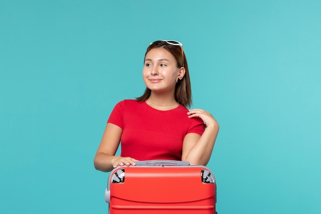Vorderansicht junge Frau mit roter Tasche, die für Urlaub auf hellblauem Raum bereit macht