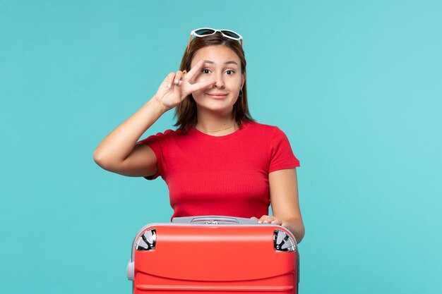 Vorderansicht junge Frau mit roter Tasche, die für Urlaub auf hellblauem Raum vorbereitet
