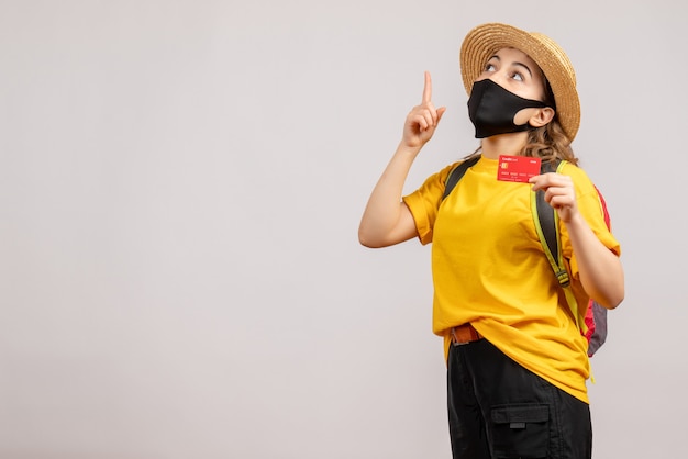 Vorderansicht junge Frau mit schwarzer Maske, die Karte hält, die mit dem Finger nach oben zeigt