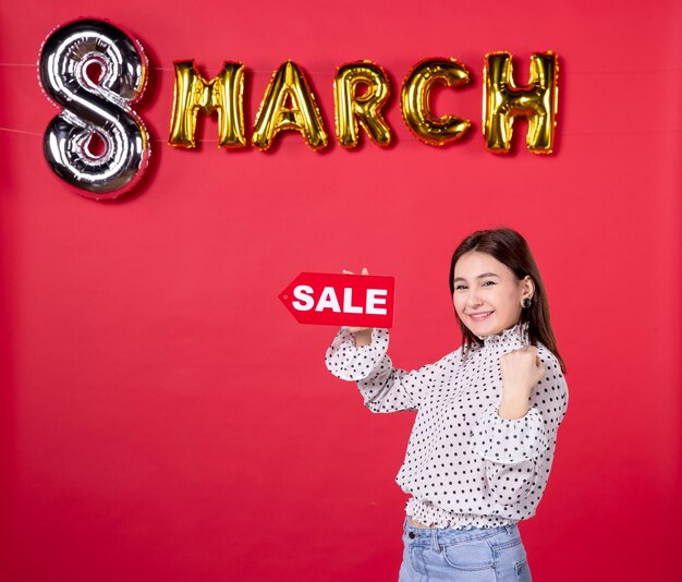 Vorderansicht junge Frau mit Verkauf Typenschild im März dekoriert roten Hintergrund Shopping Liebe liebevolle horizontale Frau Urlaub weibliche Schönheit