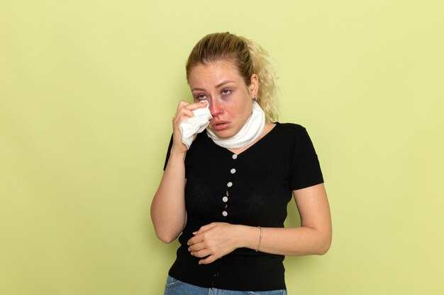 Vorderansicht junge Frau mit weißem Handtuch um ihren Hals, der sehr krank und krank auf hellgrüner Wandkrankheit Krankheit weibliches Gesundheitsmädchen fühlt