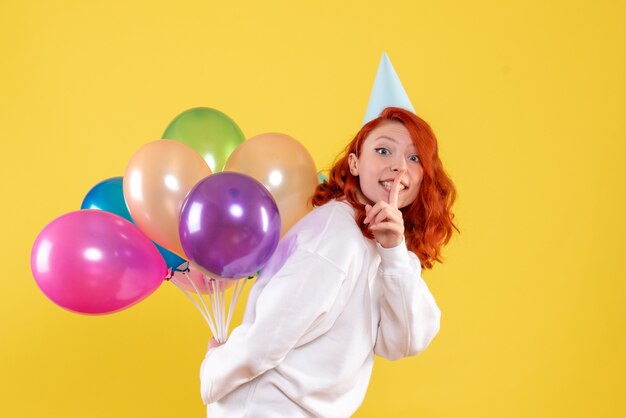 Vorderansicht junge Frau versteckt niedliche bunte Luftballons auf einem gelben Hintergrund Neujahrsfarbe Emotion Geschenk Kind Frau