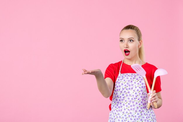 Vorderansicht junge Hausfrau, die Besteck hält und mit jemandem an der rosa Wand interagiert