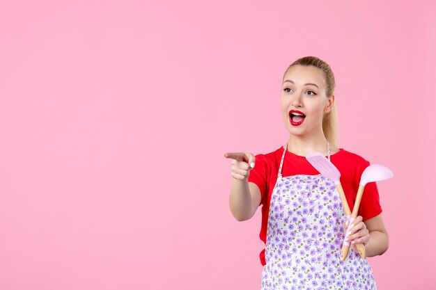 Vorderansicht junge Hausfrau, die Besteck hält und mit jemandem an der rosa Wand interagiert