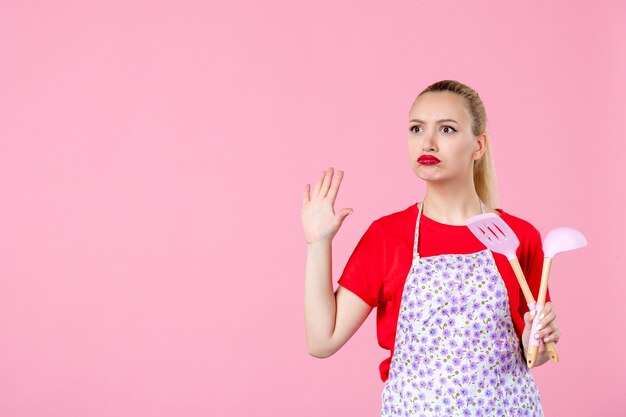 Vorderansicht junge Hausfrau, die Besteck hält und mit jemandem auf rosa Wand spricht