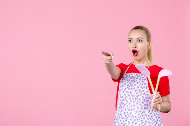 Vorderansicht junge Hausfrau mit Besteck an rosa Wand