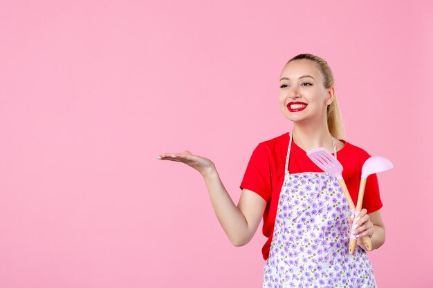 Vorderansicht junge Hausfrau mit Besteck an rosa Wand