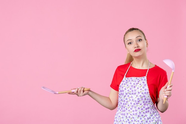 Vorderansicht junge Hausfrau mit Besteck an rosa Wand