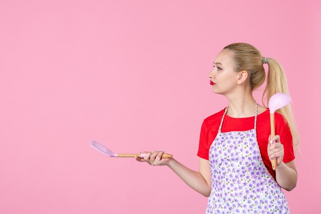 Vorderansicht junge Hausfrau mit Besteck an rosa Wand