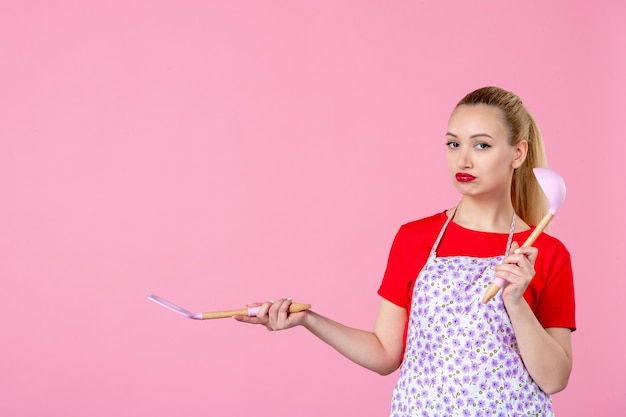 Vorderansicht junge Hausfrau mit Besteck an rosa Wand