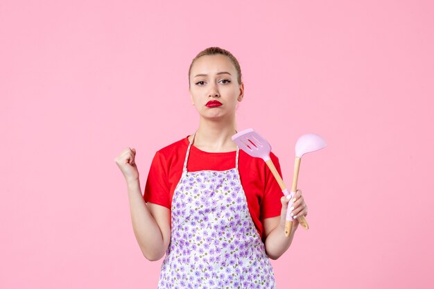 Vorderansicht junge Hausfrau posiert mit Besteck in den Händen auf rosa Wand