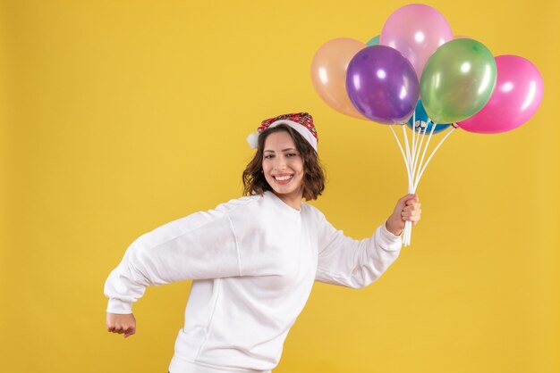 Vorderansicht junge hübsche Frau, die bunte Luftballons auf gelbem Neujahrsgefühlsfrauenfarbweihnachten hält