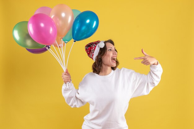 Vorderansicht junge hübsche Frau, die Luftballons auf gelbem Weihnachtsfrauen-Neujahrsfarbgefühl hält