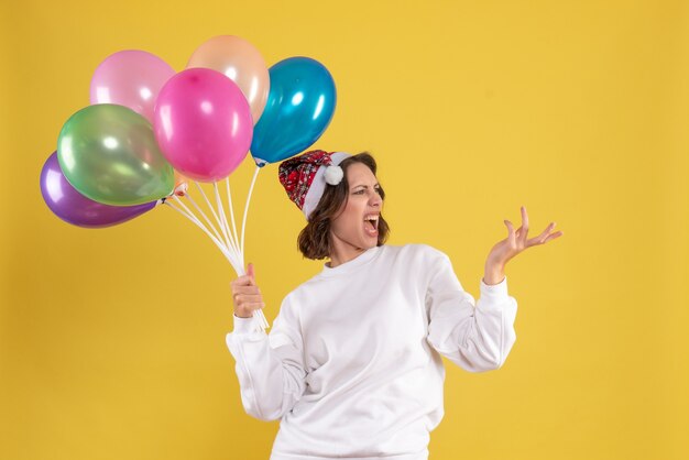 Vorderansicht junge hübsche Frau, die Luftballons auf gelber Farbe Weihnachten Neujahr Emotion Frau hält