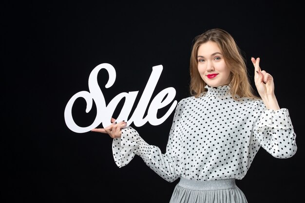 Vorderansicht junge hübsche Frau mit Verkauf schreiben auf schwarzer Wand Shopping Schönheit Mode Emotionen Farbmodell Foto