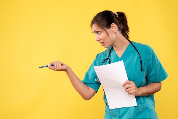 Vorderansicht junge Ärztin im medizinischen Hemd mit Papieren auf gelbem Hintergrund