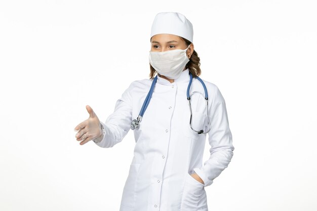 Vorderansicht junge Ärztin im weißen medizinischen Anzug und mit Maske wegen Coronavirus auf hellweißer Oberfläche