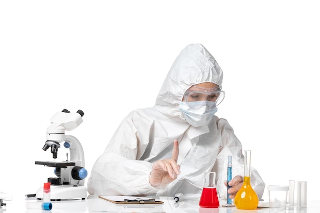 Vorderansicht junge Ärztin im weißen Schutzanzug mit Maske wegen Covid Holding blaue Lösung auf weißem Hintergrund Splash Virus Pandemie Covid