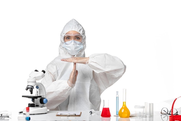Vorderansicht junge Ärztin im weißen Schutzanzug mit Maske wegen Covid zeigt t Brief auf weißem Hintergrund Virus Pandemie Splash Covid-