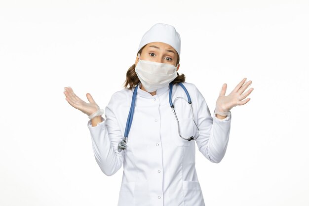 Vorderansicht junge Ärztin mit steriler Maske und Schutzhandschuhen wegen Coronavirus auf weißer Oberfläche