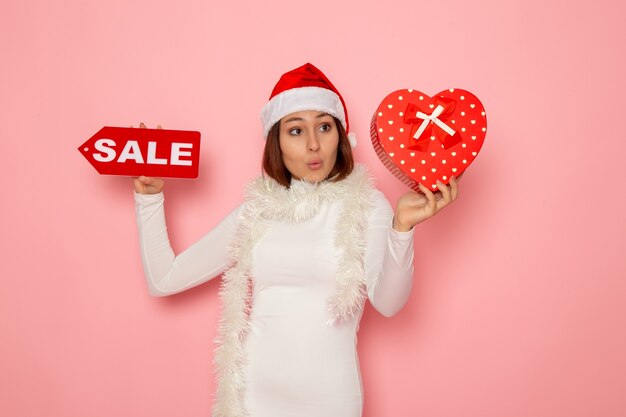 Vorderansicht junge weibliche Holding Verkauf schreiben und präsentieren auf rosa Wand Urlaub Neujahr Mode Schnee Weihnachten