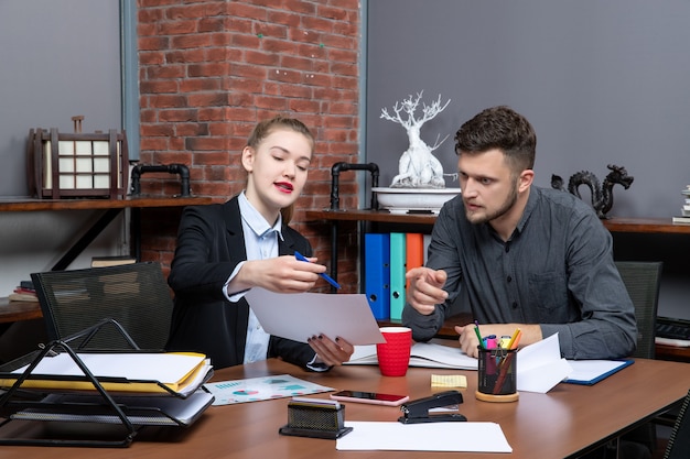 Vorderansicht junger beschäftigter Büroangestellter, die ein wichtiges Thema in dem Dokument im Büro diskutieren