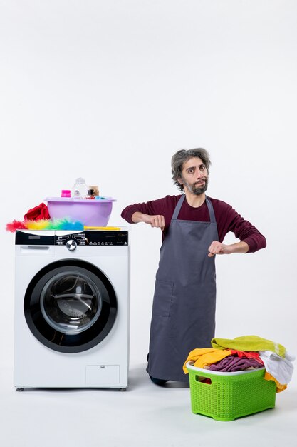 Vorderansicht junger Haushälter Mann kniet in der Nähe von Waschmaschine auf weißer Wand
