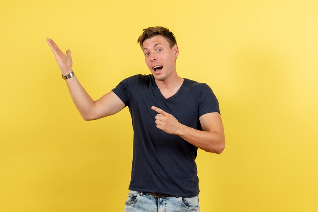 Vorderansicht junger hübscher mann in dunklem t-shirt und jeans, die auf gelbem hintergrund männliches farbmodell emotionen menschlich aufwerfen