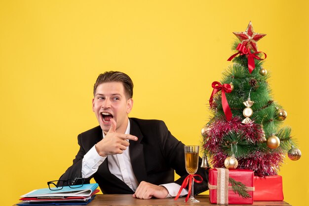 Vorderansicht junger männlicher Arbeiter, der mit Weihnachtsgeschenken und Baum sitzt