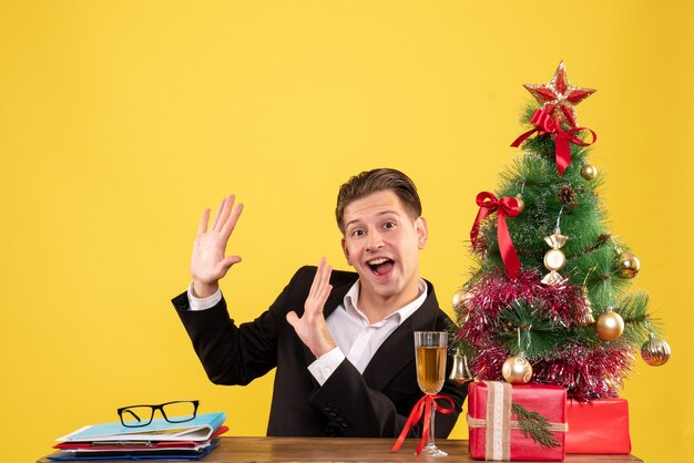 Vorderansicht junger männlicher Arbeiter, der mit Weihnachtsgeschenken und Baum sitzt