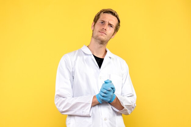Vorderansicht junger männlicher Arzt auf gelbem Hintergrund menschliche Covid Medic Pandemie