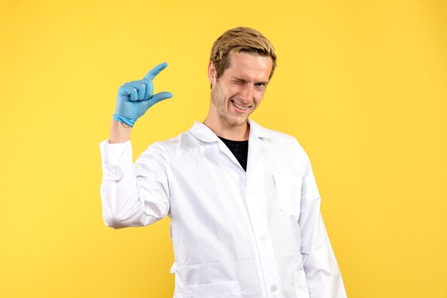 Vorderansicht junger männlicher Arzt zwinkert auf gelbem Hintergrund menschliche Covid Medic Pandemie