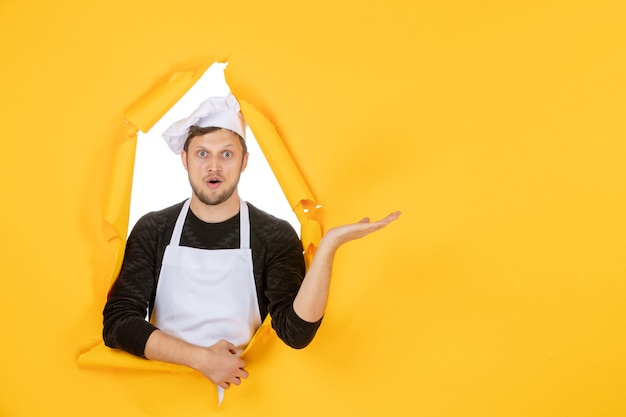 Vorderansicht junger männlicher Koch in weißem Umhang und Mütze auf gelbem, zerrissenem Hintergrund Essen Job weißer Küchenmann Küche Fotofarbe