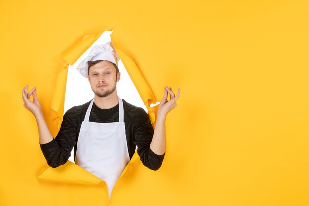 Vorderansicht junger männlicher Koch in weißem Umhang und Mütze, der auf gelbem Hintergrund meditiert Essen Job weißer Mann Küche Foto Farbe Küche