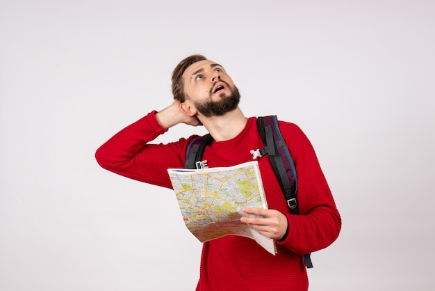 Vorderansicht junger männlicher Tourist mit Rucksack, der Karte auf weißem Wandflugzeugstadtferien-Emotion menschlicher Farbtourismus erkundet