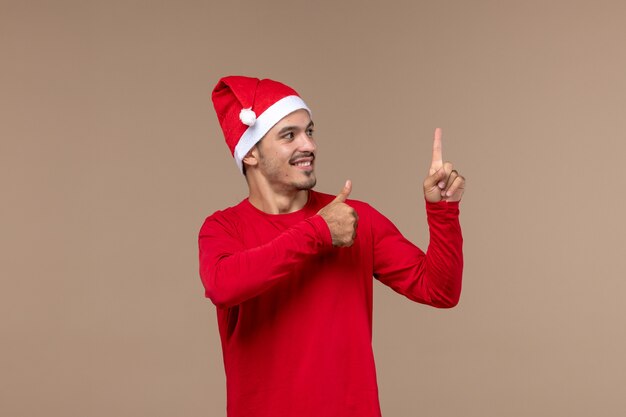 Vorderansicht junger Mann, der auf braunem Hintergrundweihnachtsemotionsfeiertagsmännchen lächelt