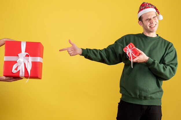 Vorderansicht junger Mann, der auf das Geschenk in der weiblichen Hand auf Gelb zeigt