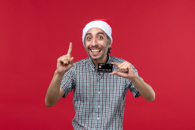 Vorderansicht junger Mann, der Bankkarte mit Lächeln auf rotem Hintergrund hält