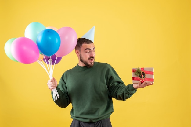 Vorderansicht junger Mann, der bunte Ballons hält und auf gelbem Hintergrund präsentiert