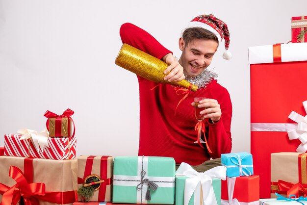 Vorderansicht junger Mann, der Champagner gießt, der um Weihnachtsgeschenke sitzt