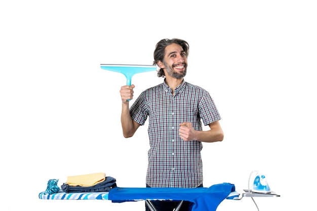 Vorderansicht junger mann, der eine reinigungsbürste hinter dem bügelbrett auf weißem hintergrund hält bügelwäsche kleidung hausarbeit saubere maschine