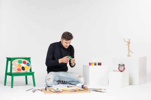 Vorderansicht junger Mann, der Farbe in einer kleinen Dose auf weißer Wand hält Fotokunst-Bildmalerei zeichnen Farbkünstlerfarben
