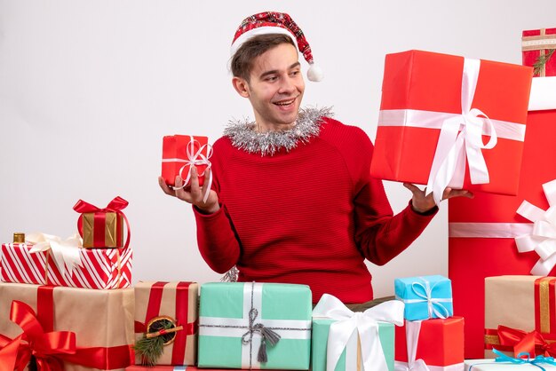 Vorderansicht junger Mann, der Geschenke betrachtet, die um Weihnachtsgeschenke sitzen