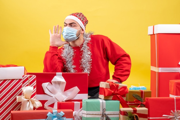 Vorderansicht junger Mann, der herum sitzt, präsentiert in Maske auf gelbem Hintergrund